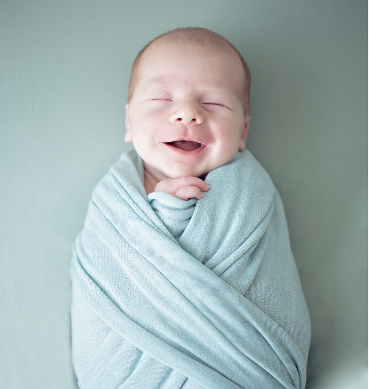 Baby Noah lächelt beim Neugeborenen-Fotoshooting in ein Pucktuch eingewickelt.